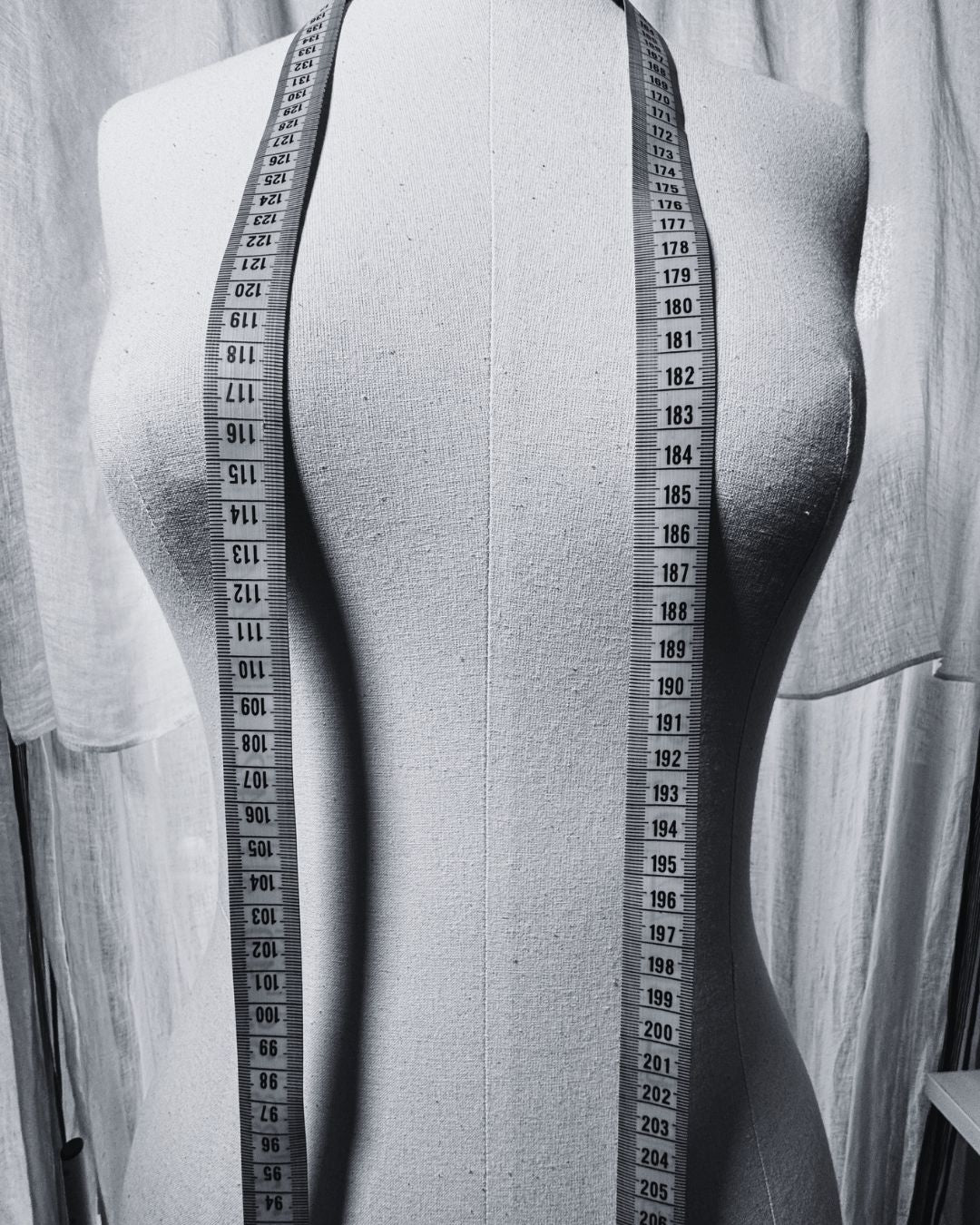 Mannequin torso with measuring tape around the waist on a plain background