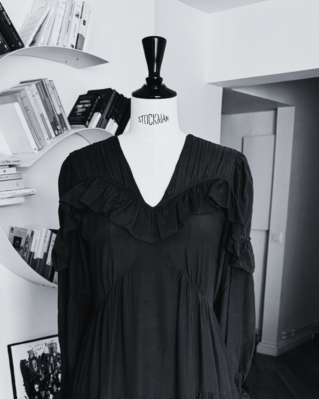 Black dress on a mannequin against a white wall with books and decor.